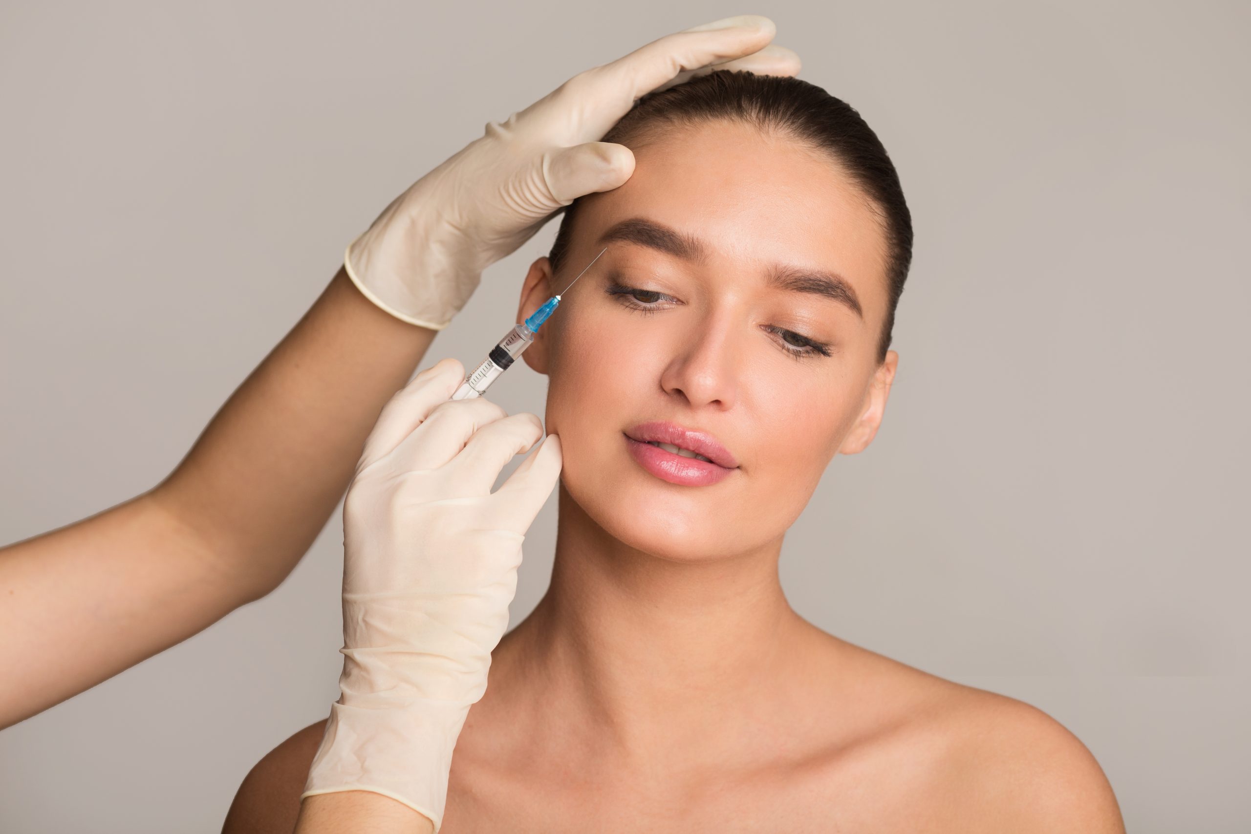 Female model with a syringe inserted into her eyebrow by gloved doctor hands
